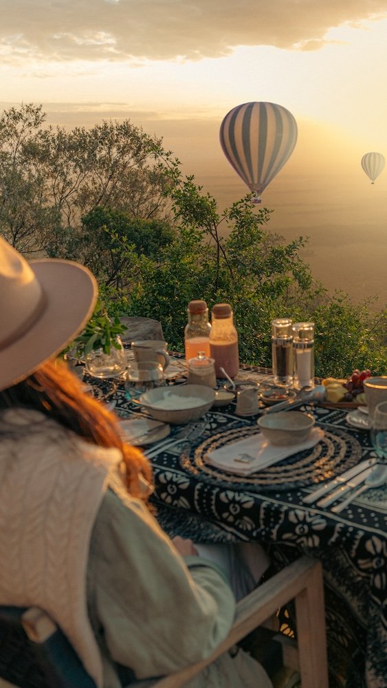 DJ mixing music at sunrise safari breakfast with hot air balloons floating over African bushland