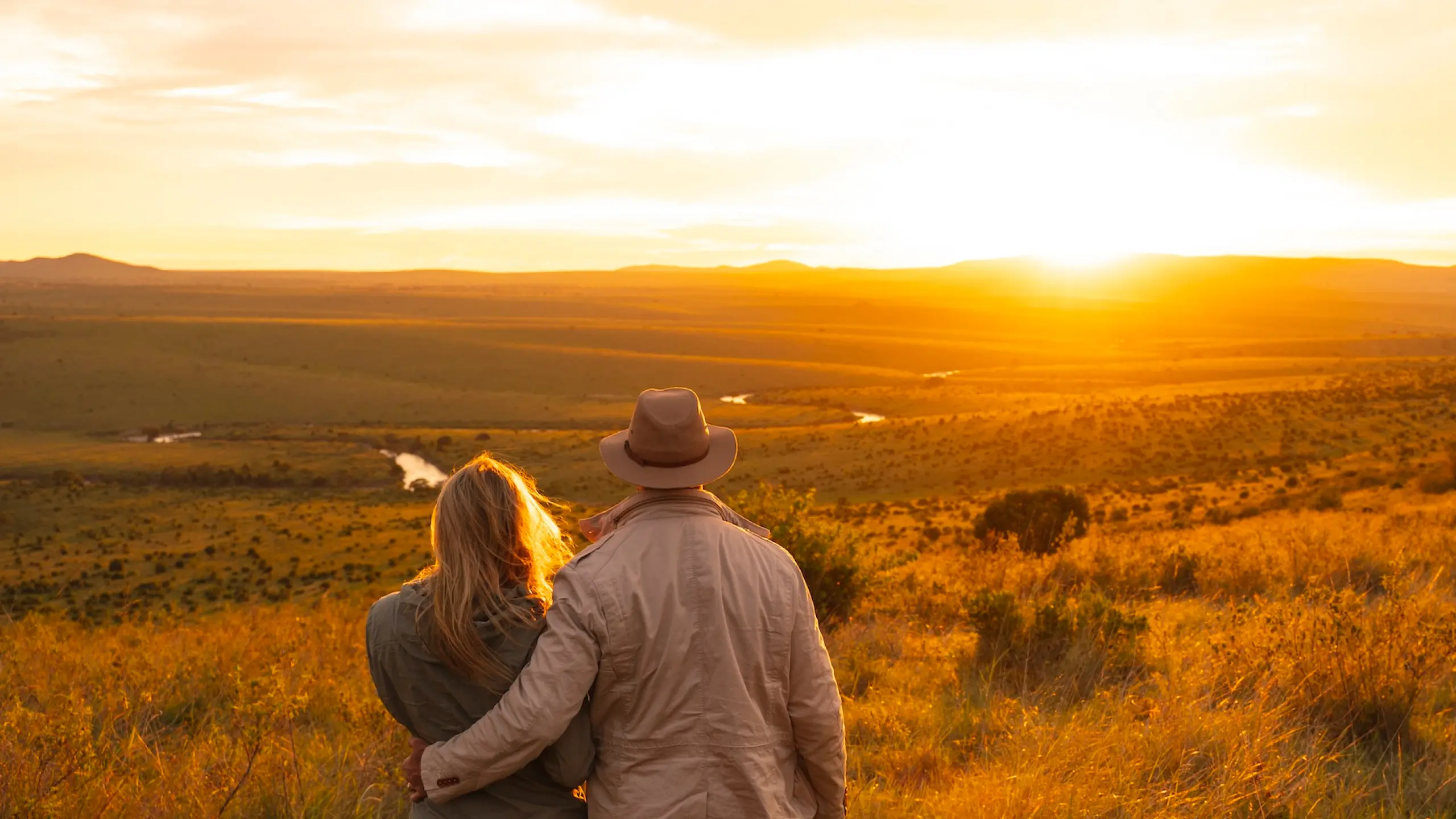 Couple viewing golden sunset over African savanna landscape during safari adventure