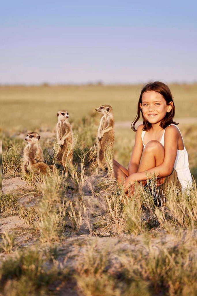 Young girl sitting with meerkats in the Kalahari Desert during a family safari adventure